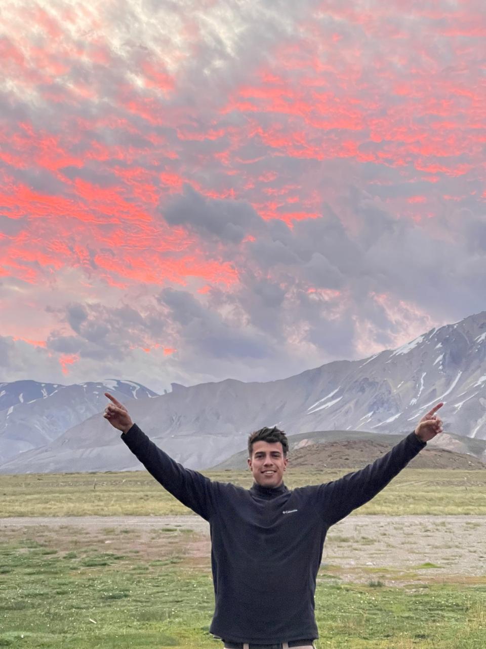 Francisco con los brazos en alto bajo un atardecer en la montaña